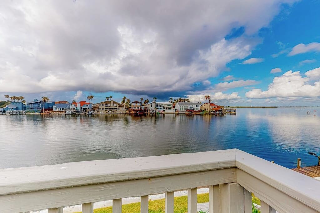 A waterfront property with a dock extending into calm water, surrounded by buildings with red roofs and palm trees.