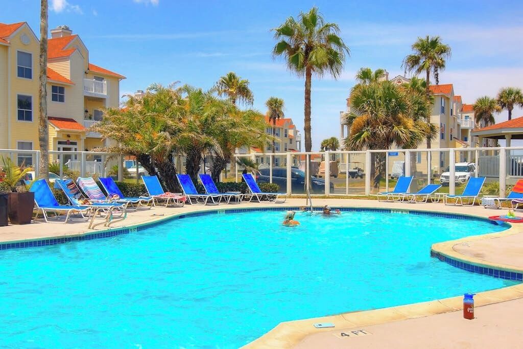 Una piscina con sillones de descanso y palmeras.