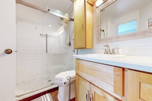 Een badkamer met een douchecabine van glas, een wit toilet, houten kastjes en een grote spiegel boven de wastafel.