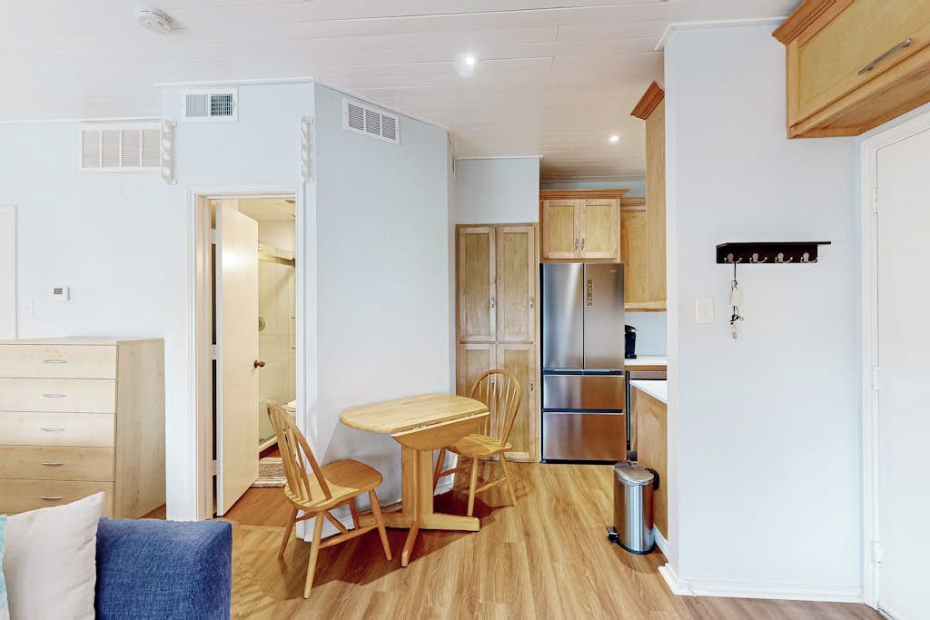 A compact kitchen with wooden cabinets, a stainless steel refrigerator, and a dining area with a wooden table and chairs.