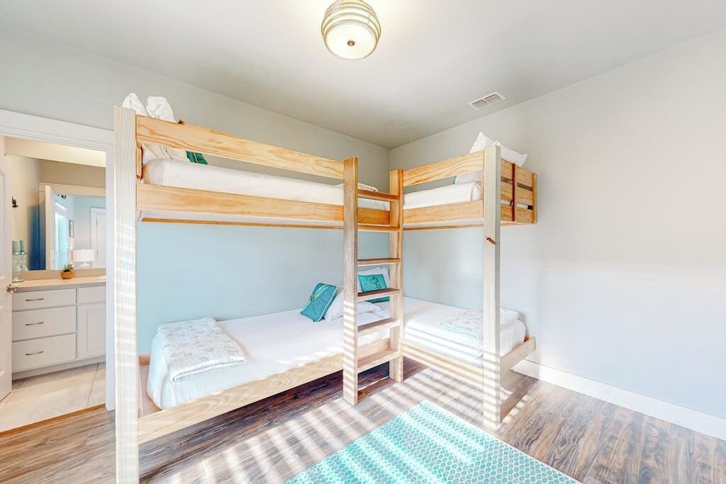 A bunk bed room with a wooden ladder, a small desk, and a mirror.