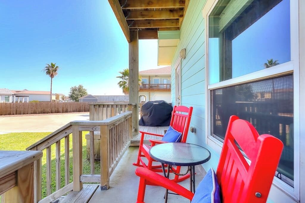 A wooden deck with a table and chairs, a covered area with a window, and a view of a residential area.