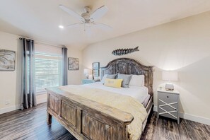 A bedroom with a wooden bed, a ceiling fan, a fish wall decoration, and a bedside table with a lamp. - Beachy Keen - Dog-Friendly with Shared Pool (Port Aransas)