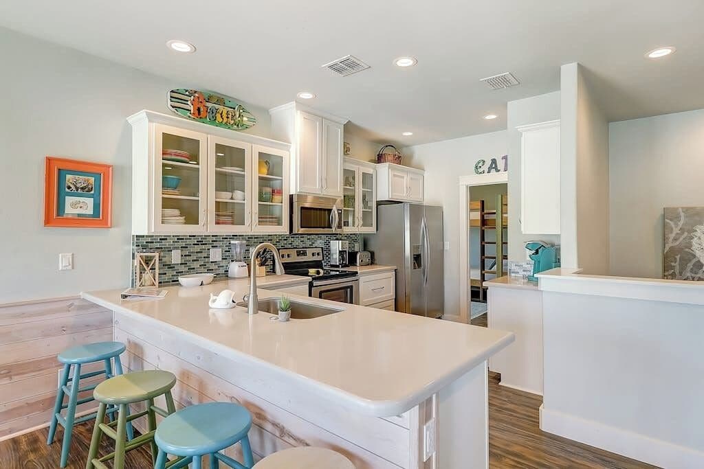 A modern kitchen with white cabinetry, a central island with stools, and a microwave above the sink.