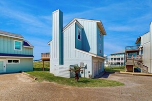 A coastal building with a garage, a small deck, and a staircase leading to a balcony. - Lost on the Sea | Lost Colony 3 - Gulf Views, Pool, Walk to Beach (Port Aransas)