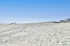 Ein weiter Sandstrand mit Fußabdrücken, einigen Personen und Gebäuden im Hintergrund.