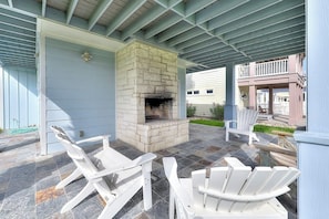 Un patio exterior con chimenea de piedra, sillas Adirondack blancas y una zona cubierta con techo de metal.