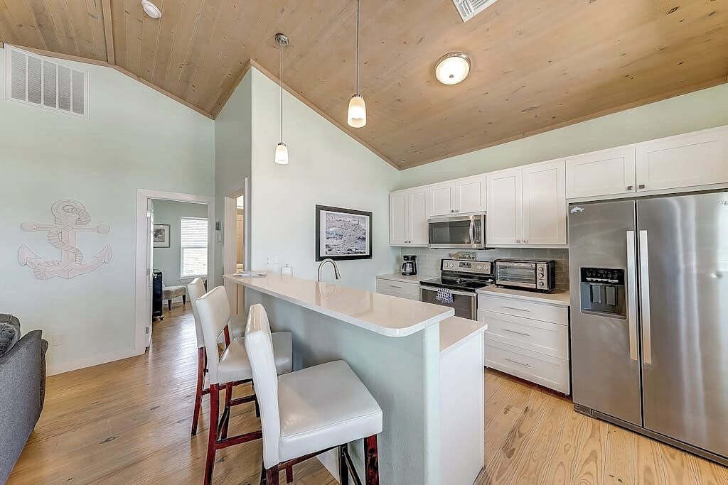 A modern kitchen with white cabinets, stainless steel appliances, and a wooden ceiling.