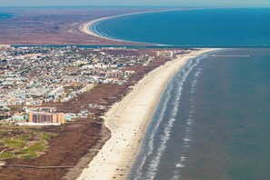 Vue aérienne d’une ville côtière, avec une longue plage, une zone résidentielle densément peuplée et un ensemble d’immeubles imposants.