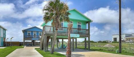A two-story house with a balcony, a palm tree, and a clear sky.