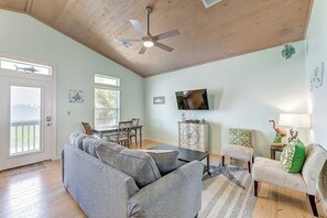Un salon doté d’un ventilateur de plafond, d’un téléviseur fixé au mur, d’un canapé, d’une table basse et d’une table d’appoint agrémentée d’objets décoratifs.