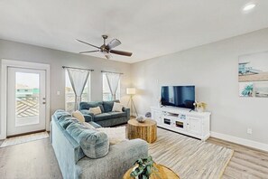 Een woonkamer met een bank, een televisie, een plafondventilator en uitzicht door een deur.