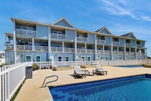 A multi-story hotel with balconies, a swimming pool, and lounge chairs. - Shoreline Retreat - Pool & Hot Tub, Walk to Beach (Port Aransas)