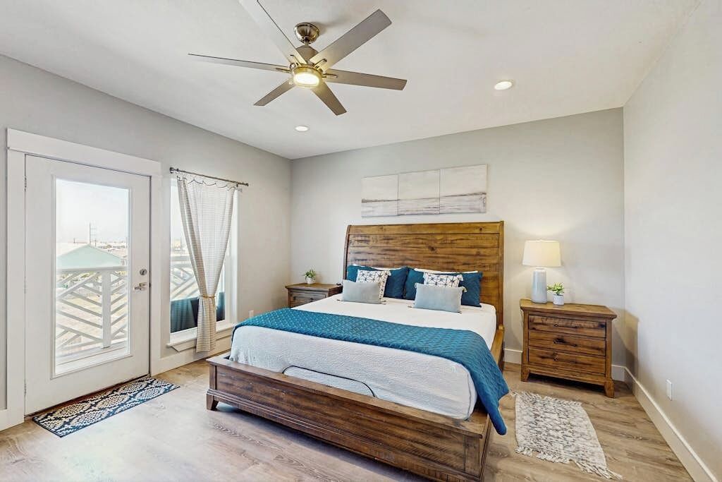Une chambre à coucher avec un lit, un ventilateur de plafond, une table de chevet, une lampe et une vue sur l’extérieur, visible à travers une porte.
