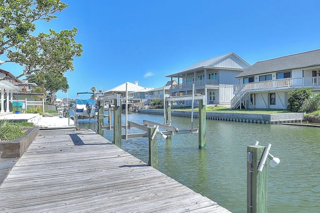 A waterfront property with a wooden dock, a marina, and a row of houses with balconies.