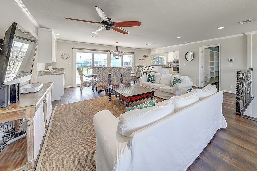 A spacious living room with a white sofa, a dining area with wicker chairs, a ceiling fan, and a view through the glass door.