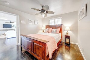 Ein Schlafzimmer mit einem hölzernen Bett, einem Deckenventilator, einem Nachttisch mit Lampe und einem Fenster mit Jalousien.