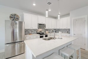 A modern kitchen with white cabinets, stainless steel appliances, a large island with bar stools, and pendant lighting. - LandsEnd - Indoor-Outdoor Living, Boat Parking (Rockport)