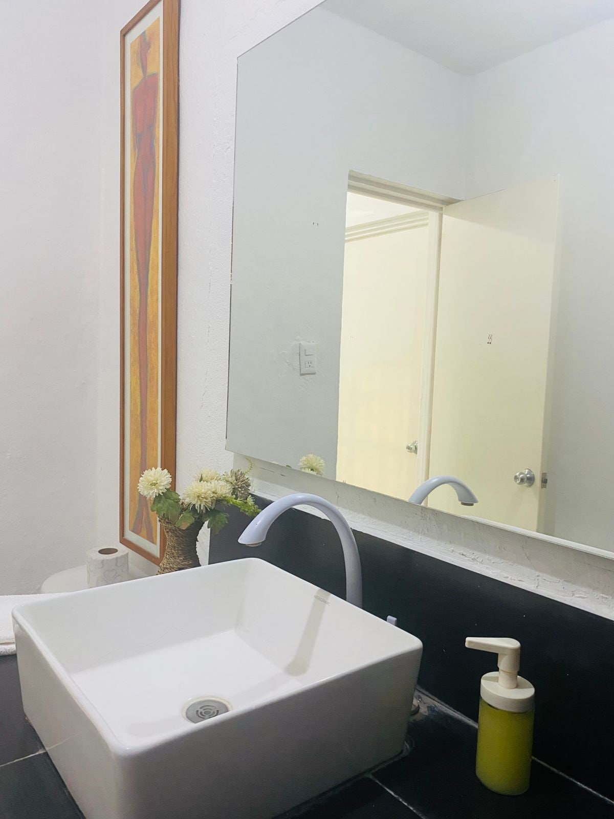 Une salle de bain avec un lavabo blanc, un miroir et un distributeur de savon jaune.