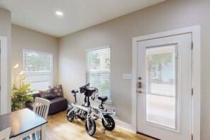 A compact living space with a dining area, a sofa, a bicycle, and a door with a window. - Three Palms By The Bay (Rockport)