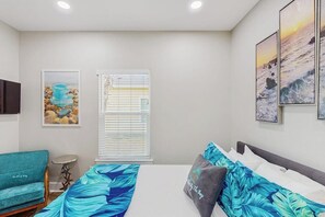 A bedroom with a bed, a sofa, a small table, and artwork on the walls. - Three Palms By The Bay (Rockport)