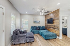 A modern living room with a sectional sofa, ottoman, and a ceiling fan. - Three Palms By The Bay (Rockport)