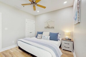Ein Schlafzimmer mit einem Bett, einem Nachttisch, einem Deckenventilator, einer Tür und einem Wandbild.