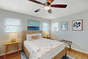 A bedroom with a bed, a ceiling fan, a nightstand with a lamp, and artwork on the wall. - Bay Breeze House - Waterfront, Dock & Hot Tub (Rockport)