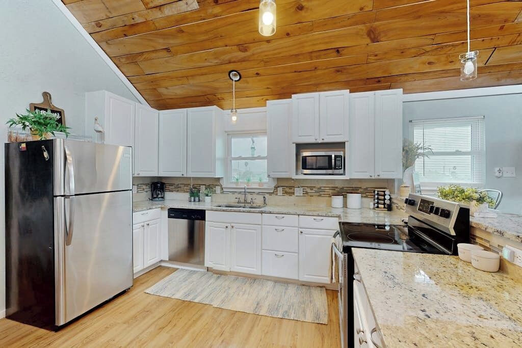 A modern kitchen with white cabinets, stainless steel appliances, and a wooden ceiling.