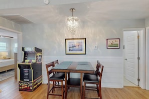 A dining area with a table and chairs, a chandelier, and a video game machine. - Bay Breeze House - Waterfront, Dock & Hot Tub (Rockport)
