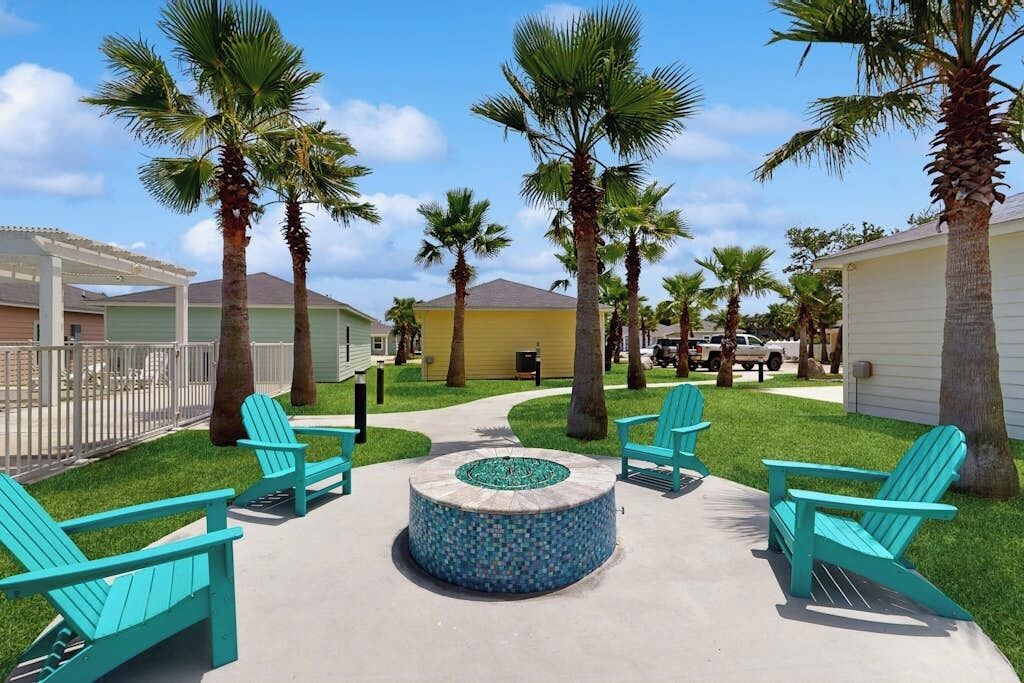 Un patio con mesas al aire libre, palmeras y una chimenea circular.