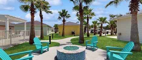Un patio con mesas al aire libre, palmeras y una chimenea circular.
