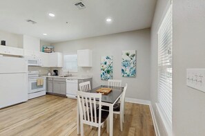 A modern kitchen with white cabinetry, a dining table with chairs, and artwork on the walls. - Rockport Rendezvous - Pool, Pond & Fire Pit (Rockport)