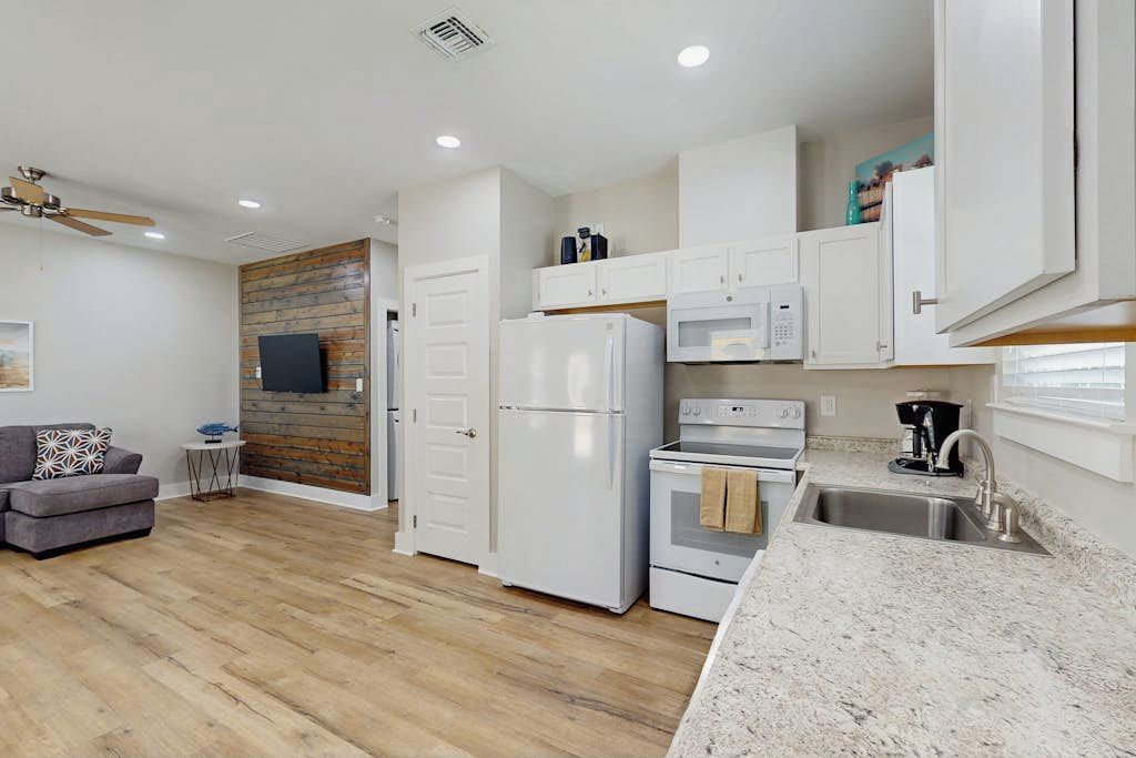 A modern kitchen with white appliances, a granite countertop, and a wooden wall.