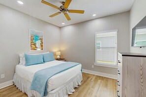 A bedroom with a bed, a ceiling fan, a nightstand with a lamp, a window with blinds, and a wooden cabinet. - Rockport Rendezvous - Pool, Pond & Fire Pit (Rockport)