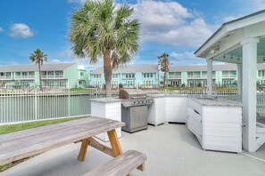 An outdoor patio with a grill, a wooden table, and a poolside area. - Belle of the Bay - Boat Slip, Pool & Tennis (Rockport)