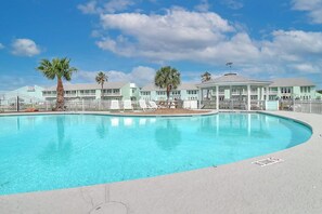 A swimming pool with a clear blue water surface, surrounded by a white fence, and a building with a light blue facade in the background. - Belle of the Bay - Boat Slip, Pool & Tennis (Rockport)