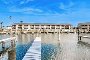 Un hotel frente al agua con varios balcones, un muelle y cielo despejado.