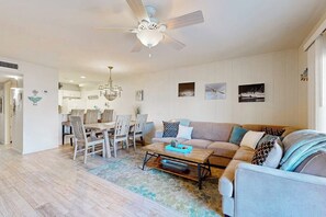 A living room with a ceiling fan, a dining area with chairs and a table, and a sofa with cushions. - Casita da la Bahia - Boat Slip & Water Views (Rockport)