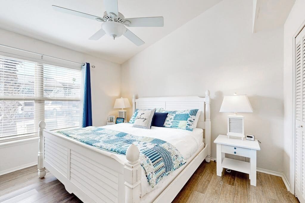 A bedroom with a bed, bedside tables, a ceiling fan, and a window with blinds.