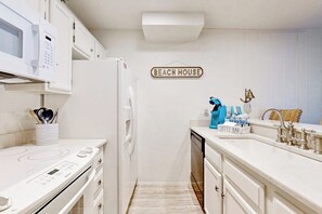 A kitchen with white cabinetry, a microwave, a refrigerator, a coffee bar, and a sign that reads 'BEACH HOUSE'. - Casita da la Bahia - Boat Slip & Water Views (Rockport)