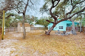 A rustic outdoor area with a blue house, wooden fence, and leaf-covered ground. - Casa Azul - Fenced Yard, Fire Pit & Dogs OK (Rockport)