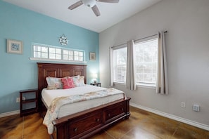 A bedroom with a wooden bed, a ceiling fan, a window with blinds, and a wall clock. - Casa Azul - Fenced Yard, Fire Pit & Dogs OK (Rockport)