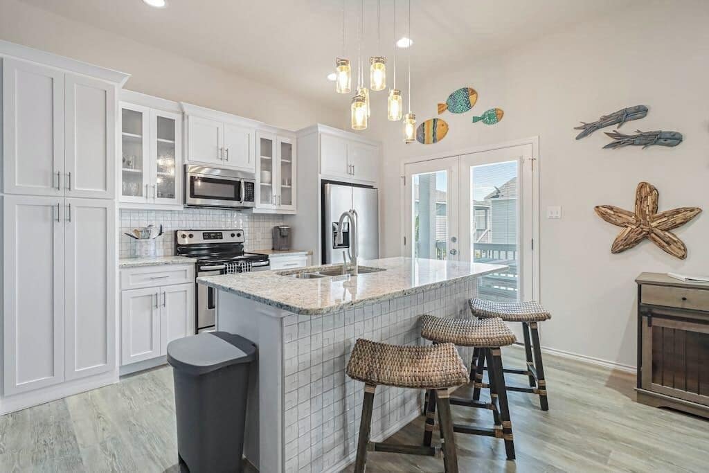 A modern kitchen with white cabinetry, a central island with stools, a stainless steel refrigerator, and a microwave.