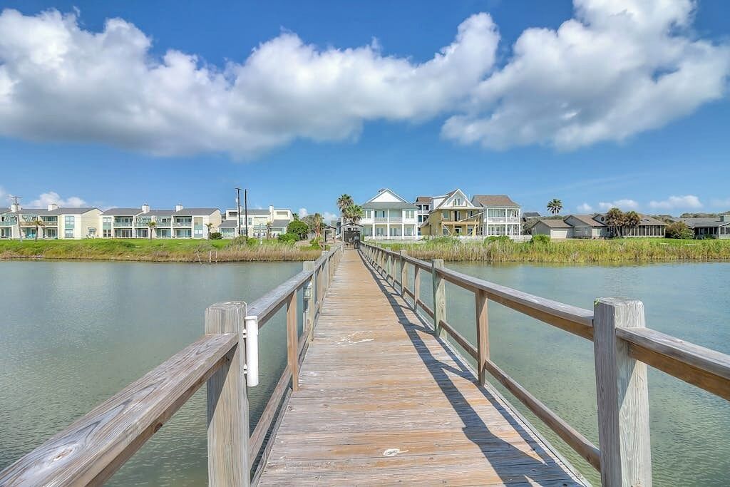A wooden pier leading to a row of houses by a calm body of water.