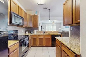 A kitchen with wooden cabinets, a microwave, stove, and granite countertops. - Cay Getaway - Private Balcony & Shared Pool (Corpus Christi)