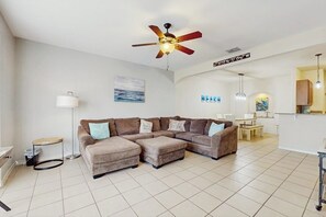 A modern living room with a sectional sofa, a ceiling fan, and a dining area in the background. - Cay Getaway - Private Balcony & Shared Pool (Corpus Christi)