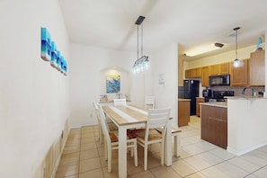 A modern kitchen with wooden cabinets, a central island, and a dining area with a wooden table and chairs. - Cay Getaway - Private Balcony & Shared Pool (Corpus Christi)