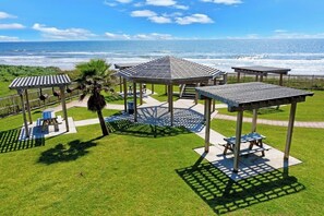 A gazebo with a roof, surrounded by a well-maintained lawn, and a view of the ocean. - Seascape Condos - Day Break at the Seascape #2219 (Galveston)