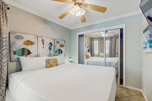 Ein Schlafzimmer mit einem Bett, einem Deckenventilator, einer Wand mit einem Fisch-Motiv und einer Tür zu einem anderen Raum.